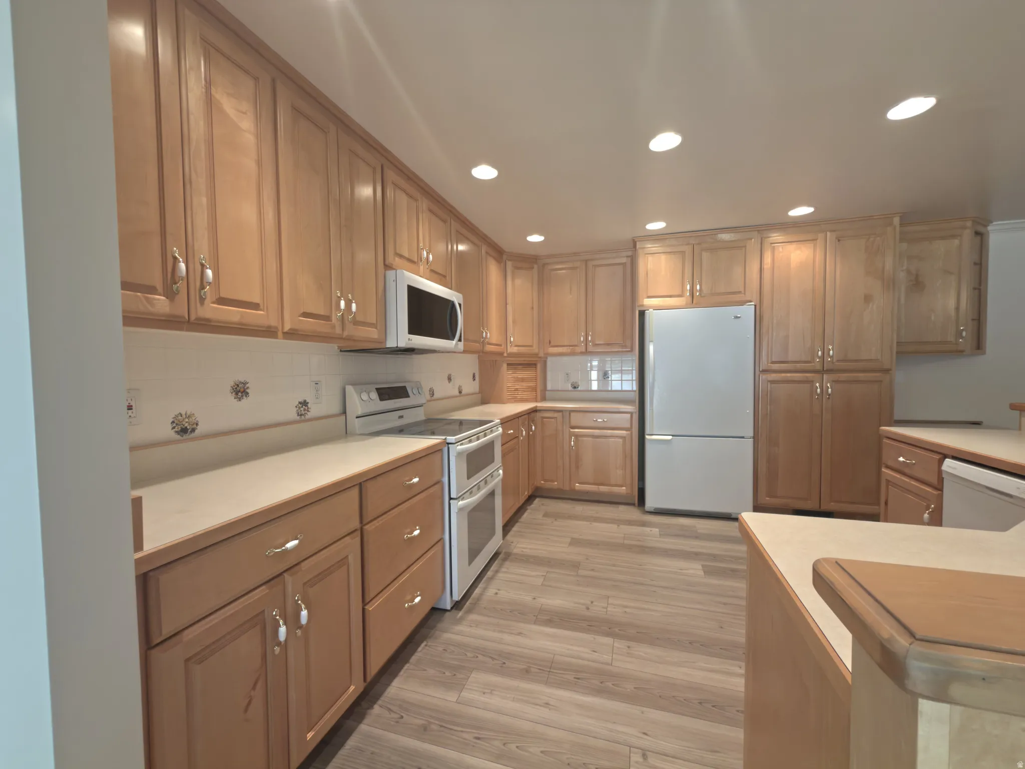 Kitchen featuring extensive light wood cabinetry, light countertops, wood-finish flooring, white appliances, and recessed lighting