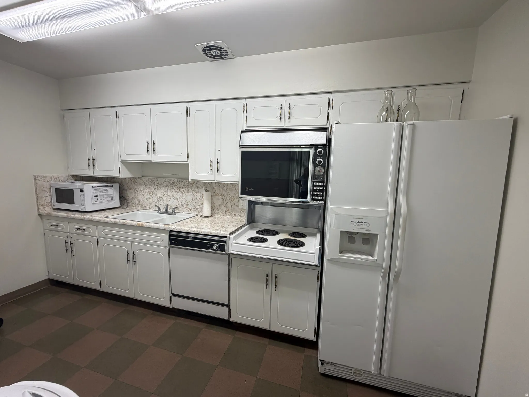Club House Kitchen featuring white cabinetry with dark hardware, a double basin sink, and a built-in oven with an electric cooktop