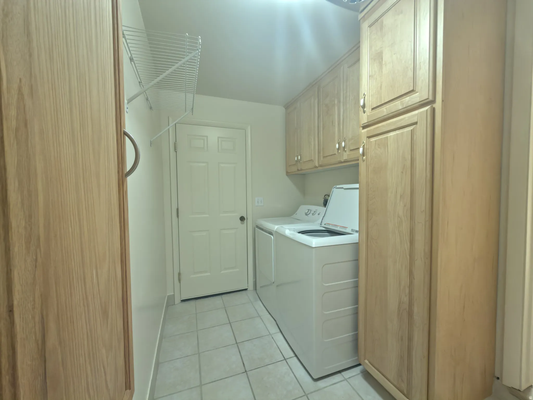 Laundry room featuring square tile flooring, wood-finish cabinetry, upper storage cabinets, and a wire shelving unit