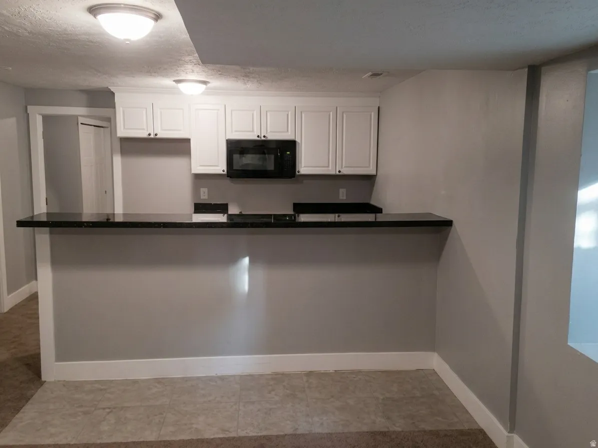 Kitchenette featuring white cabinetry, black microwave, and dark countertops