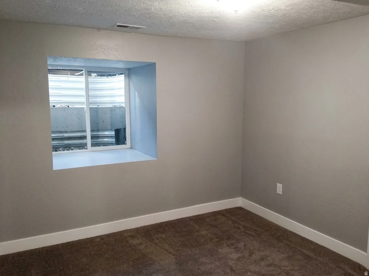 Neutral-toned room featuring a window well, light gray walls, white baseboards, and brown carpeting