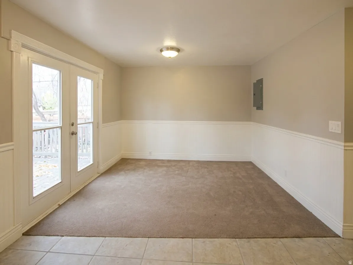 Room featuring glass-paneled French doors, wainscoting, and neutral carpet