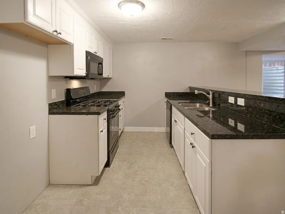 Galley kitchen featuring white cabinetry, dark speckled countertops, and a full suite of black appliances