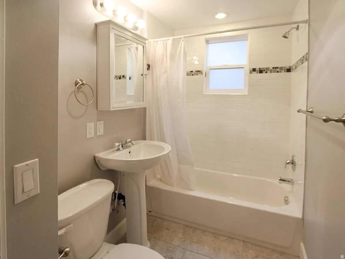 Bathroom featuring a pedestal sink, white subway tile shower surround with an accent band, a built-in tub, and a window