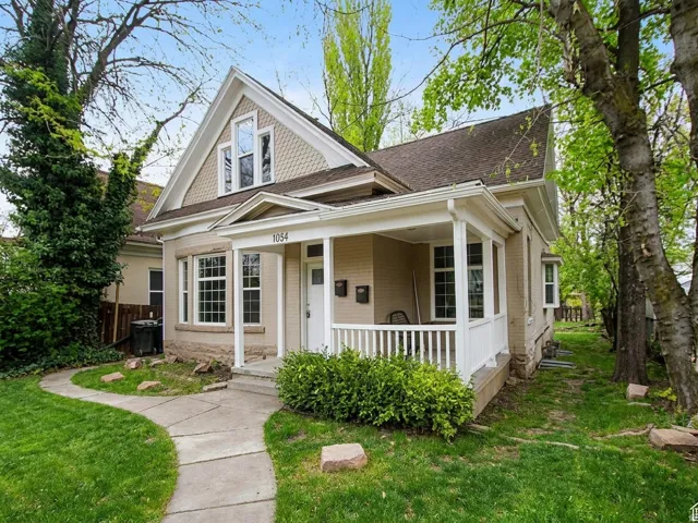 Exterior featuring a covered porch with white railings, a curved concrete pathway, and a prominent second-story dormer with decorative shingle siding
