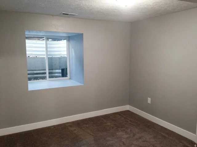 Neutral-toned room featuring a window well, light gray walls, white baseboards, and brown carpeting