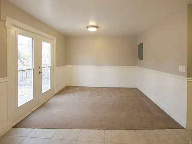 Room featuring glass-paneled French doors, wainscoting, and neutral carpet
