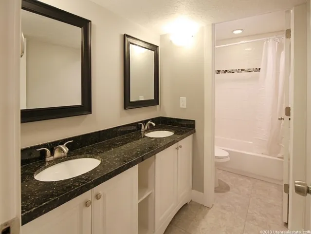 Bathroom featuring a dual vanity with dark speckled countertops, white cabinetry, and undermount sinks