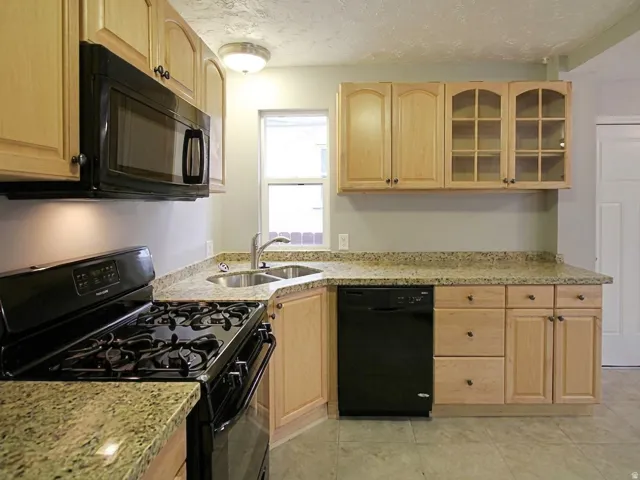 Kitchen featuring light wood cabinetry, stone-finish countertops, and black appliances