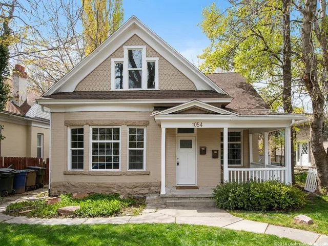 Traditional residential facade featuring a covered porch, white balustrade, and a prominent gable with decorative shingles