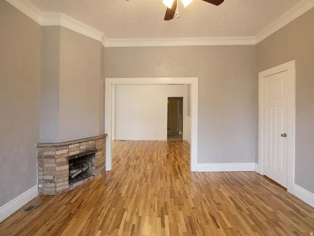 Interior space featuring wood-finish flooring, a brick fireplace, and crown molding