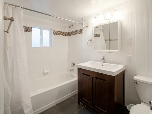 Bathroom featuring a white subway tile surround with decorative accent band, a white bathtub, and dark tile flooring