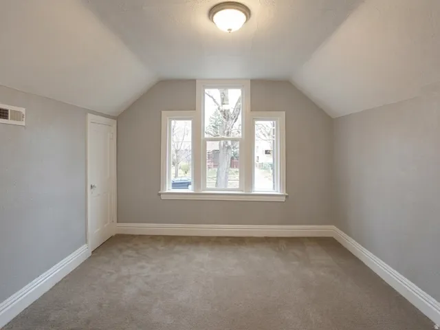 Carpeted room featuring sloped ceilings and a flush-mount ceiling light fixture