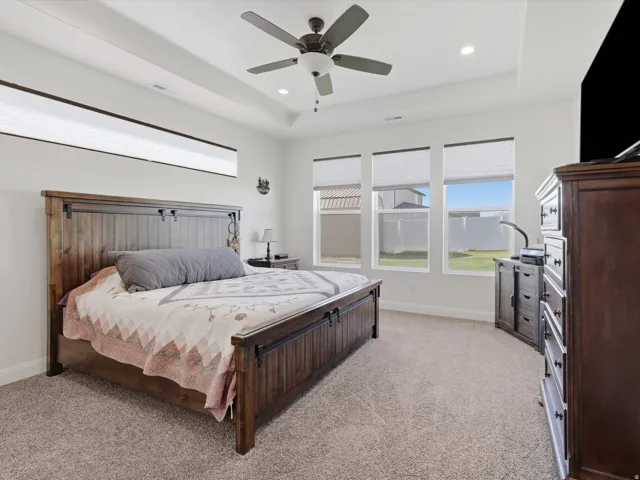 Master bedroom with tray ceiling, recessed lighting and a ceiling fan, complemented by high-set transom windows