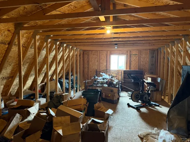 Unfinished loft space above garage featuring exposed wood framing and ceiling-mounted light fixtures