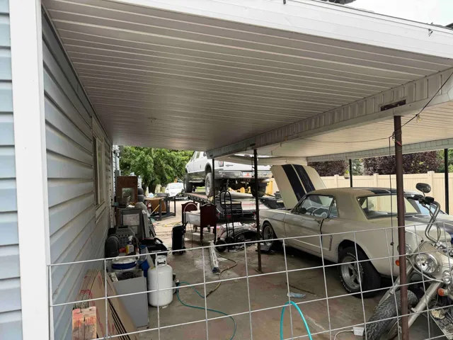 Covered carport featuring a concrete floor, light blue vinyl siding, and a white fence perimeter