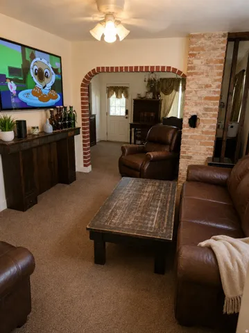 Living room featuring a carpeted floor, brick-lined arched doorway, brick accent wall, and a ceiling fan with light fixture