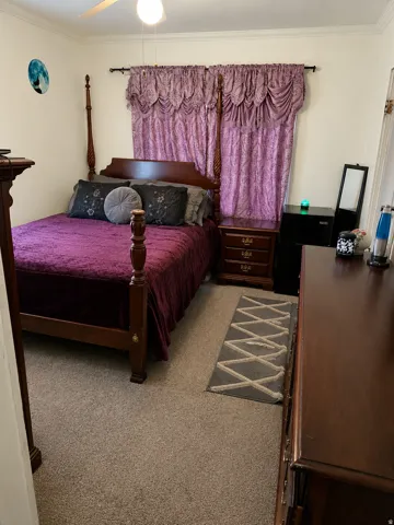 Carpeted bedroom featuring a ceiling fan with integrated lighting, crown molding, and a window with valance and drapery