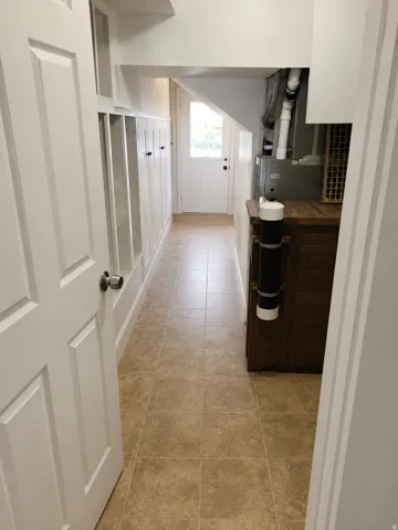 Mudroom with built-in cubbies and hooks, tiled flooring, white painted trim, white paneled door, and natural light from exterior door