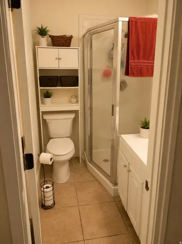 Compact bathroom featuring a corner shower with a glass enclosure, white vanity cabinetry with a built-in sink, and a commode