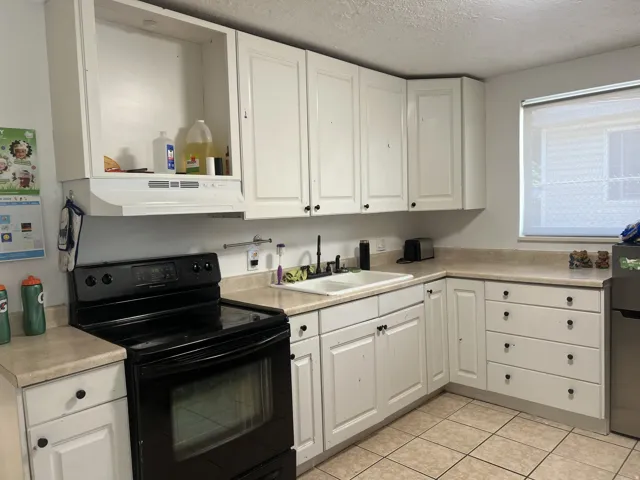 Kitchen featuring white cabinetry with black hardware, a dual basin sink, black electric range with an overhead microwave hood, and light-toned tile flooring