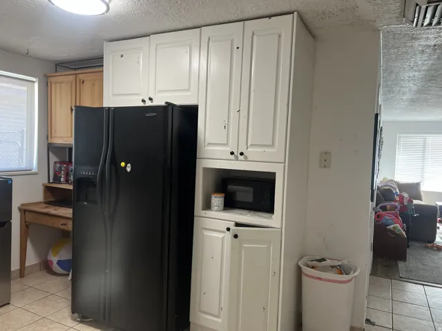 Kitchen area featuring white cabinetry, integrated microwave nook, tile flooring, and a window with blinds