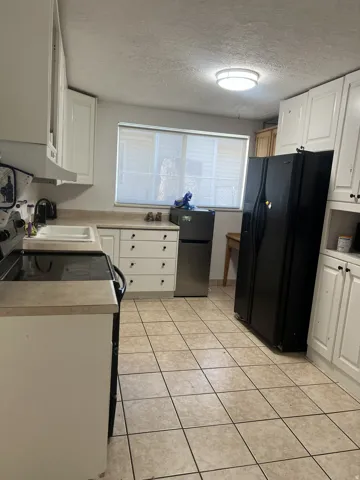 Spacious kitchen featuring tile flooring, white cabinetry, laminate countertops, a built-in sink, and a window with blinds