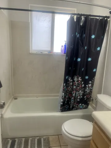 White bathtub with a curved shower rod, tile surround, and a frosted window