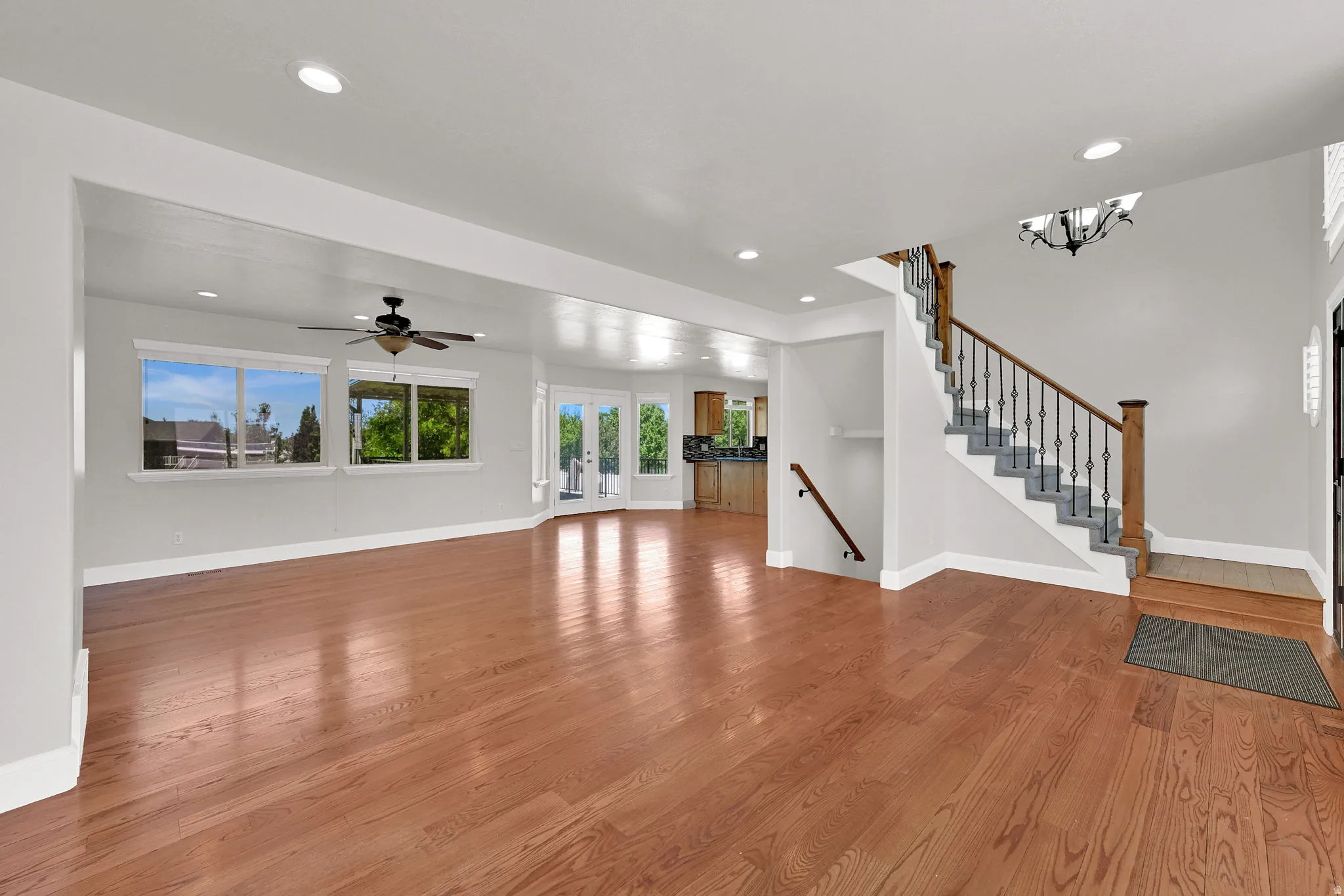 Spacious interior featuring hardwood flooring, a staircase with wrought iron balusters, recessed lighting, and multiple windows