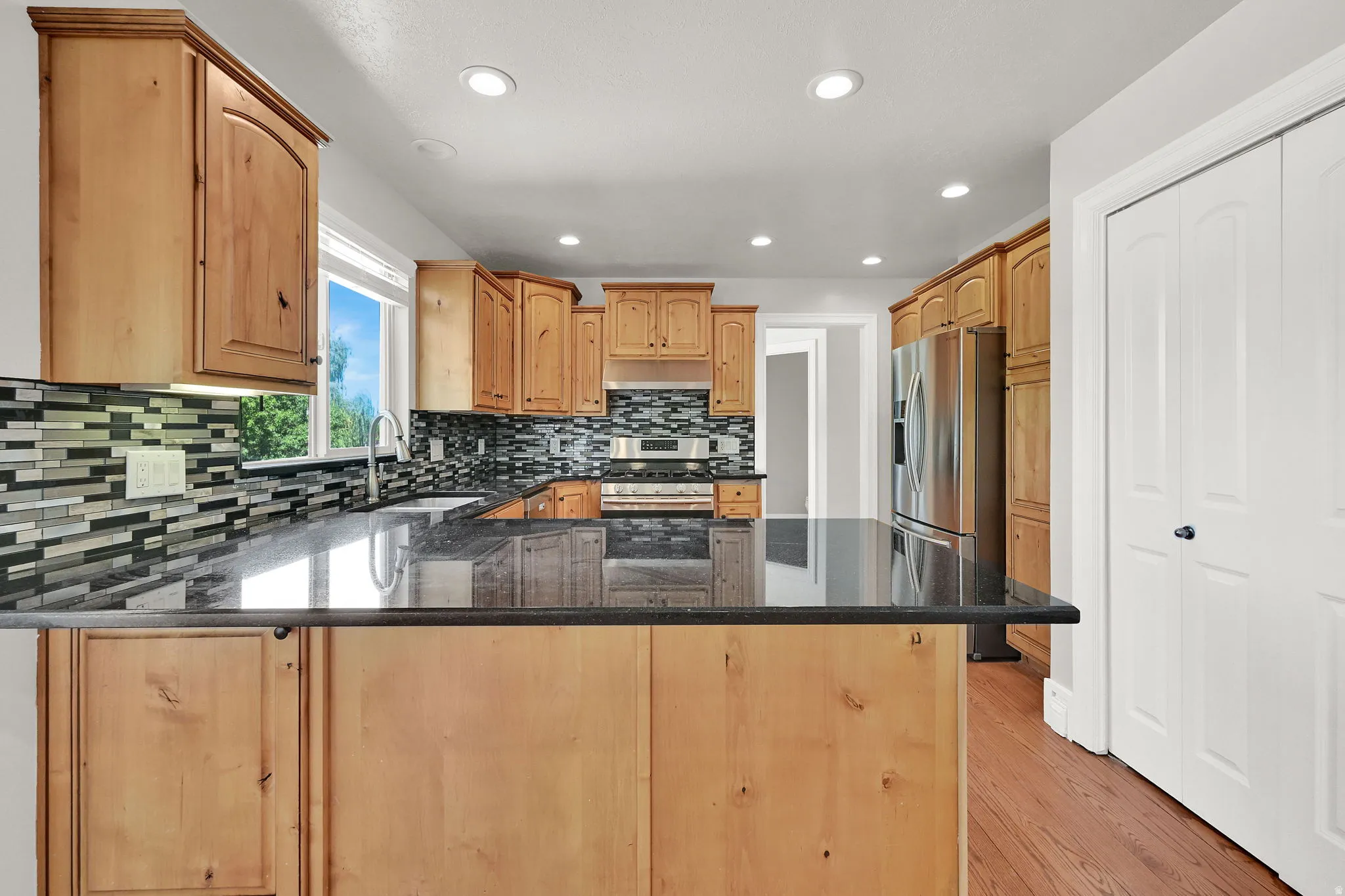 Kitchen featuring wood cabinetry, dark countertops, tile backsplash, stainless steel appliances, and recessed lighting