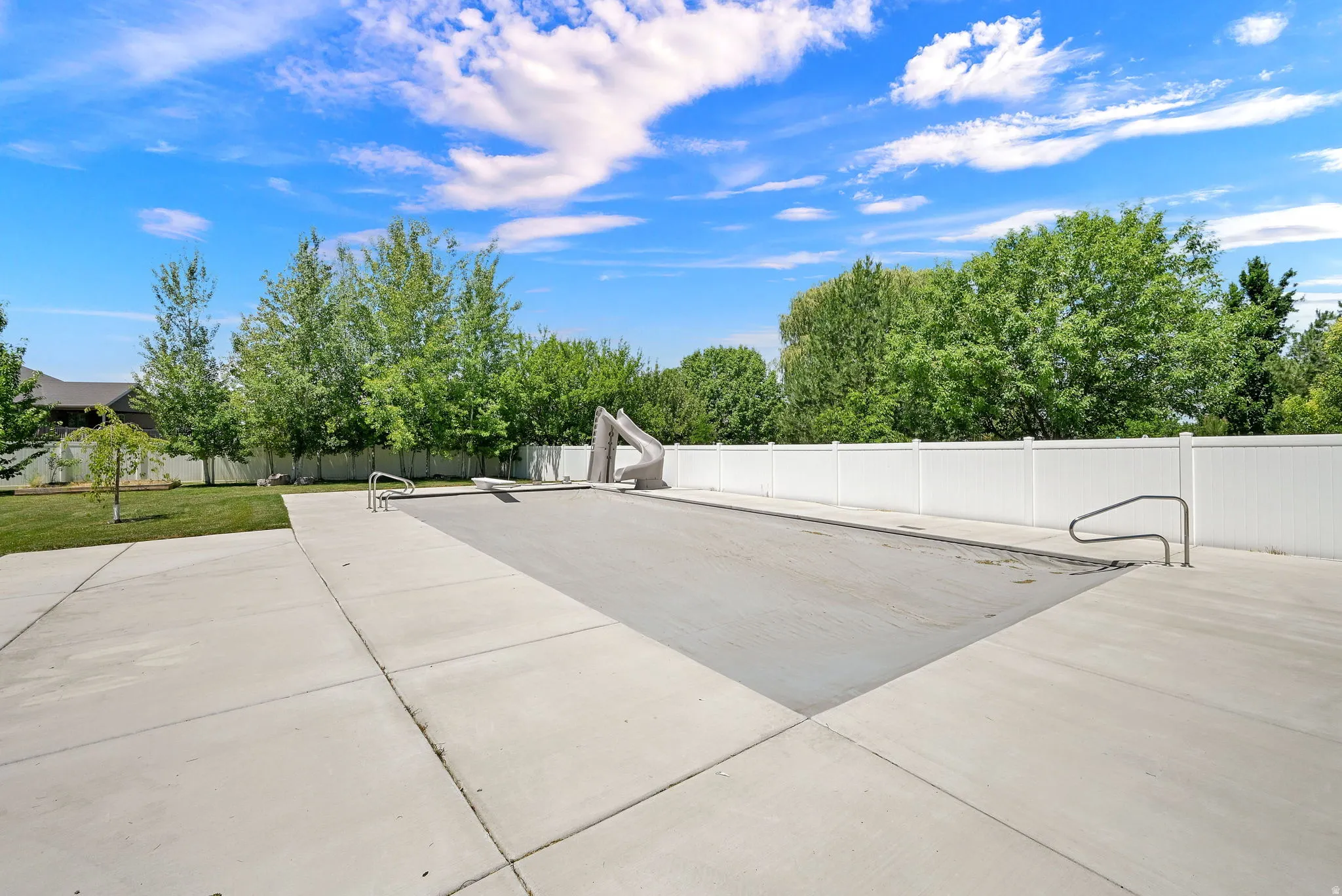Outdoor pool area featuring a covered swimming pool with an attached slide, concrete decking, and a white vinyl privacy fence