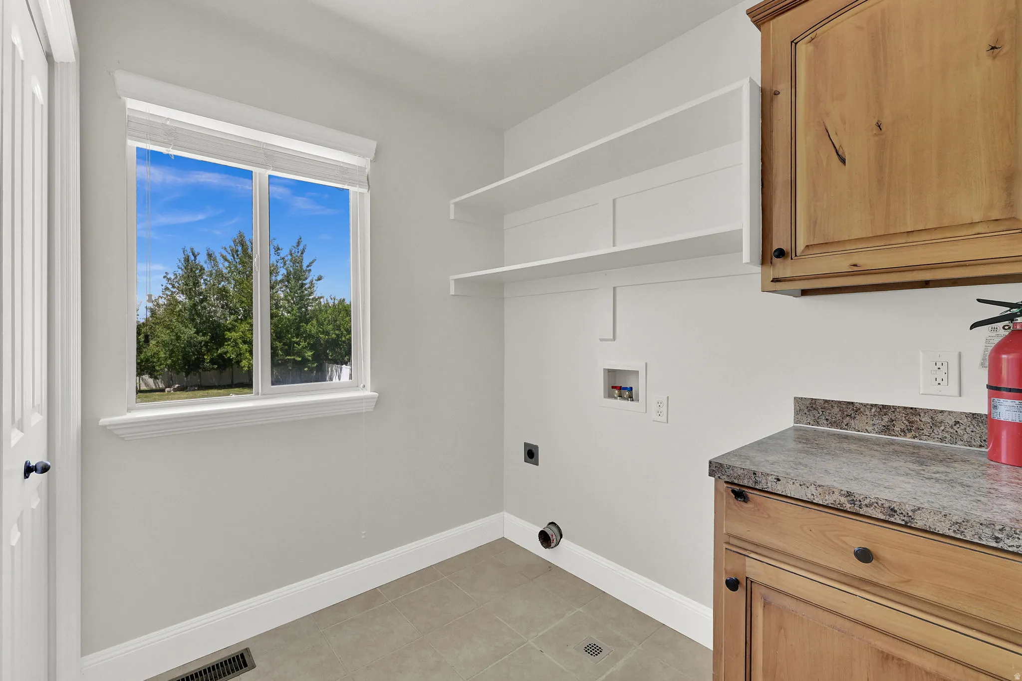 Laundry area featuring a window, built-in shelving, stone-finish countertop, and wood cabinetry