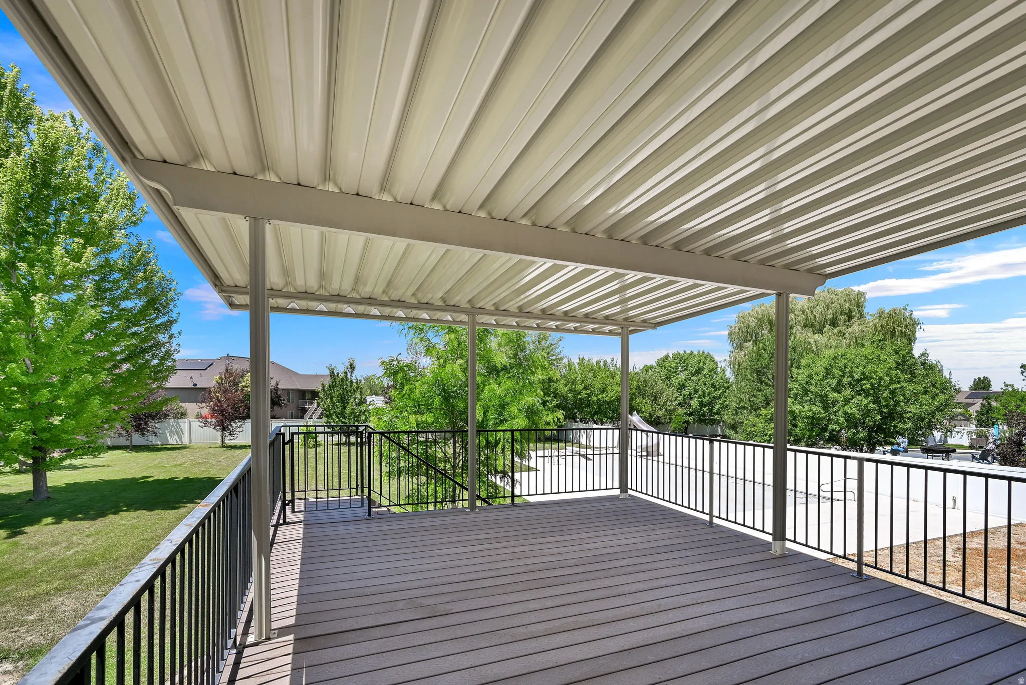 Expansive covered deck featuring composite decking, black metal railings, and a corrugated metal roof