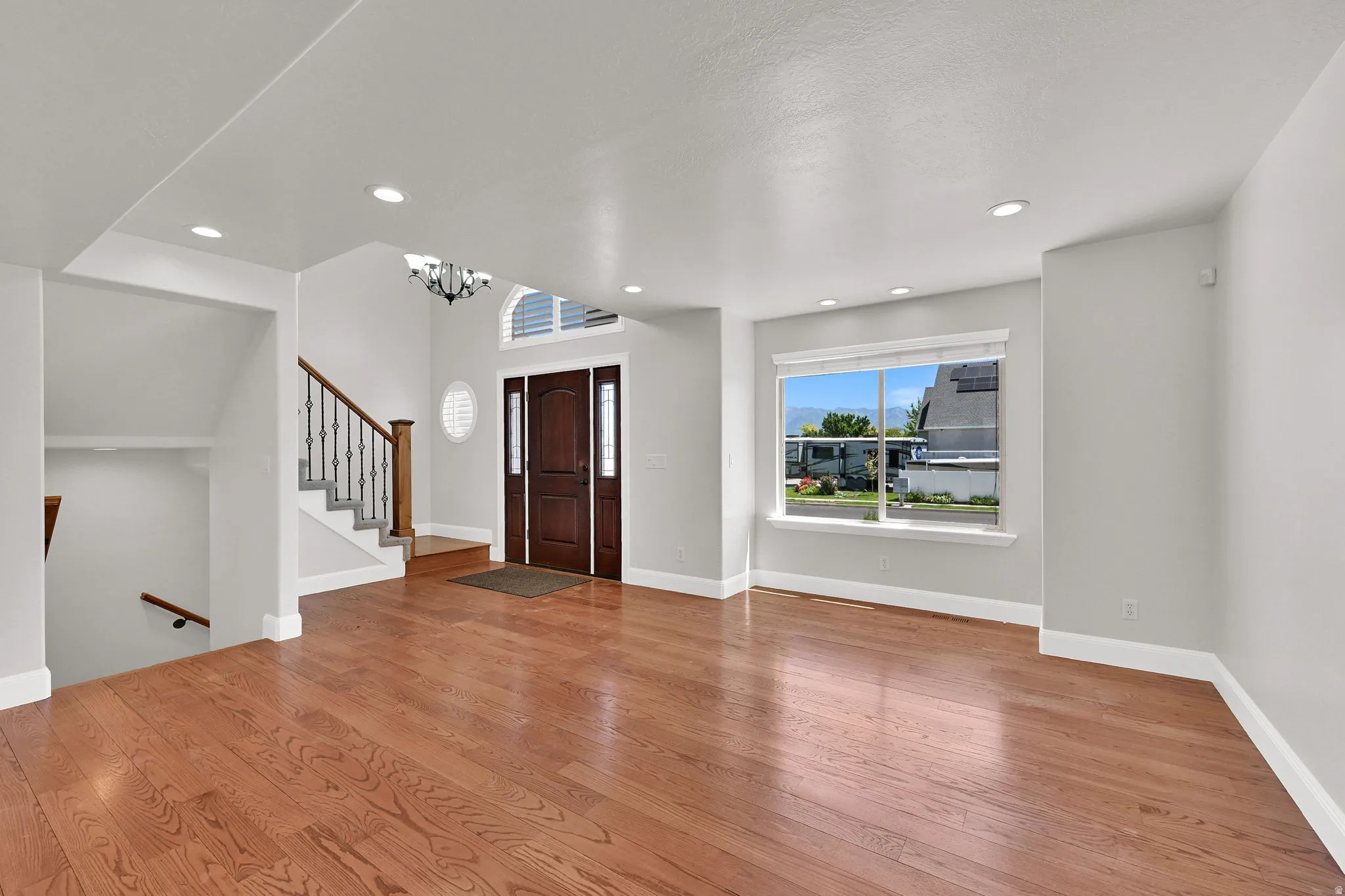 Entryway featuring wood-finish flooring, a grand staircase with dark iron balusters, a large front door with sidelights, an arched transom window, and recessed lighting