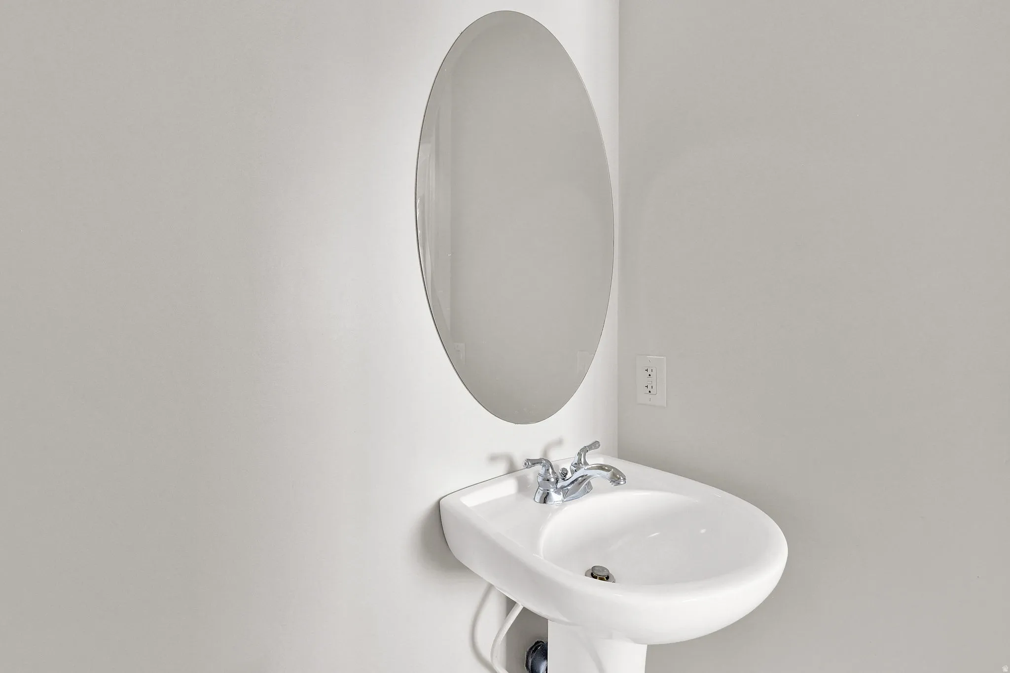Pedestal sink with chrome faucet, complemented by an oval wall-mounted mirror