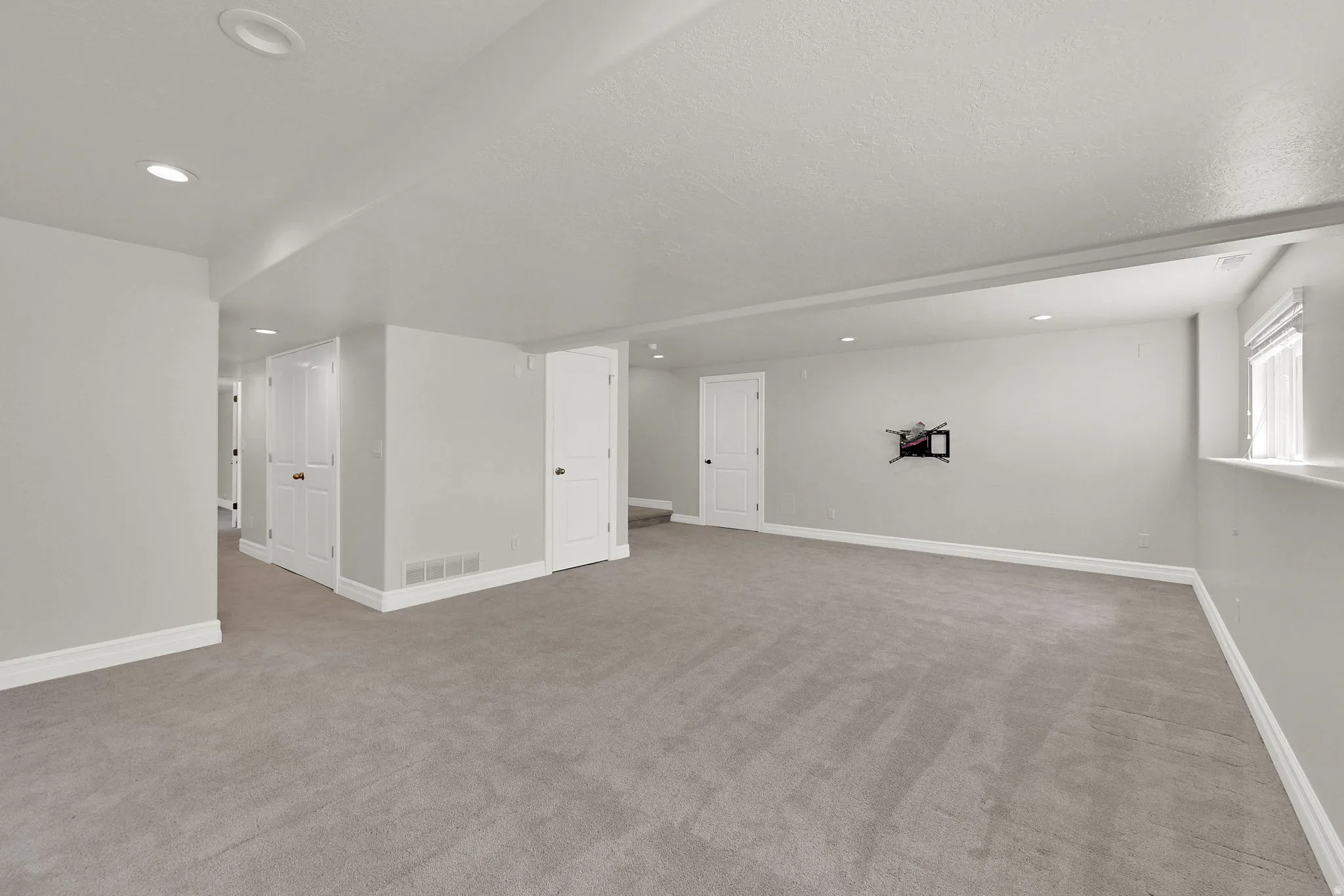 Spacious room featuring light gray carpeting, recessed lighting, white baseboards, and white interior doors