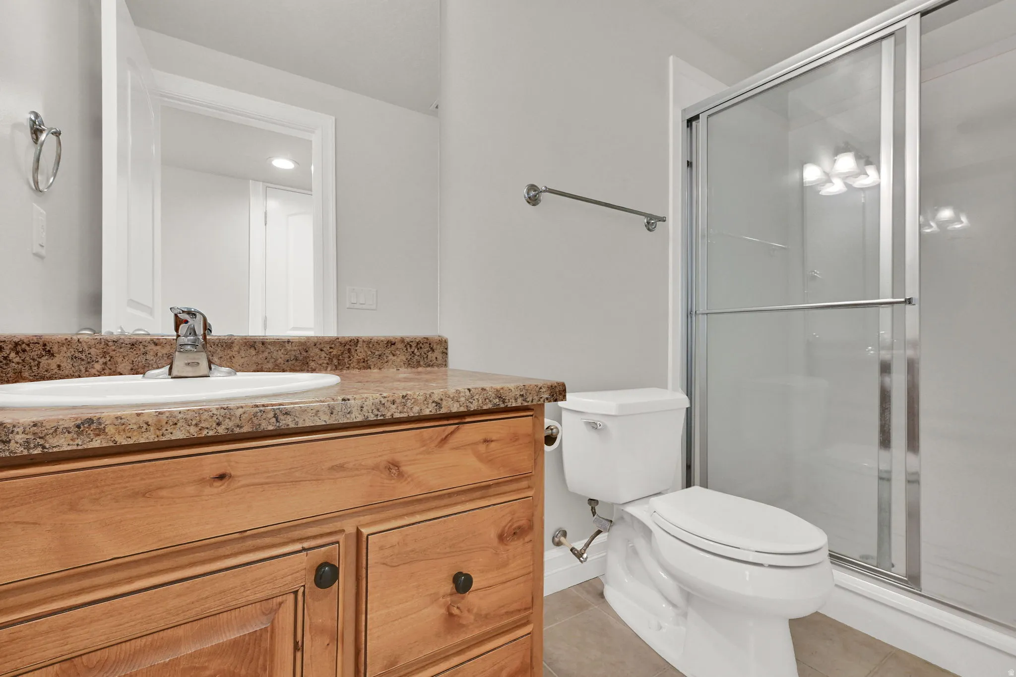 Bathroom featuring a wood vanity with an integrated sink, stone-finish countertop, stainless steel faucet, and a glass-enclosed shower with a sliding door