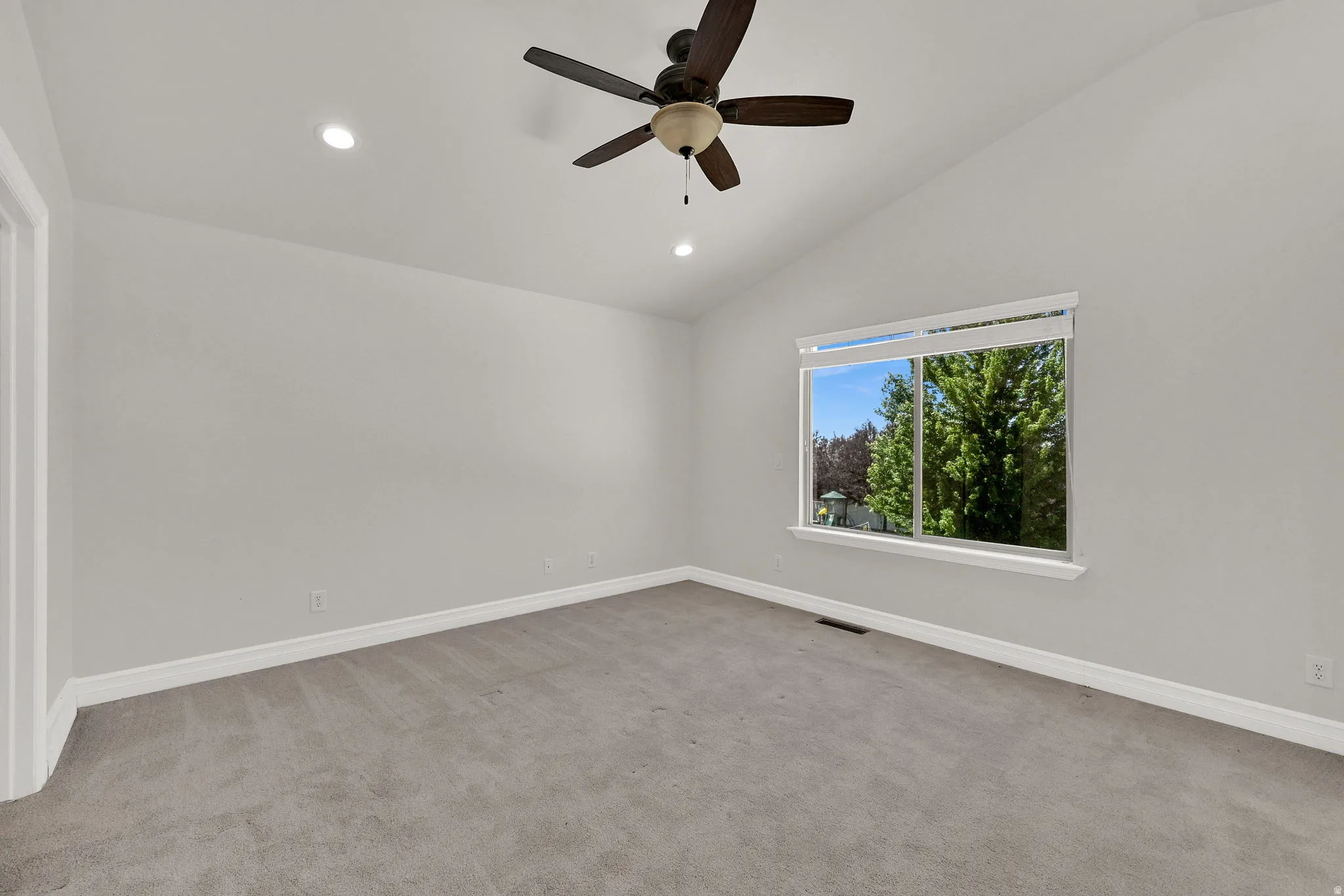 Vaulted ceiling room featuring light gray carpeting, a ceiling fan with integrated lighting, recessed lighting, and a large window with white trim