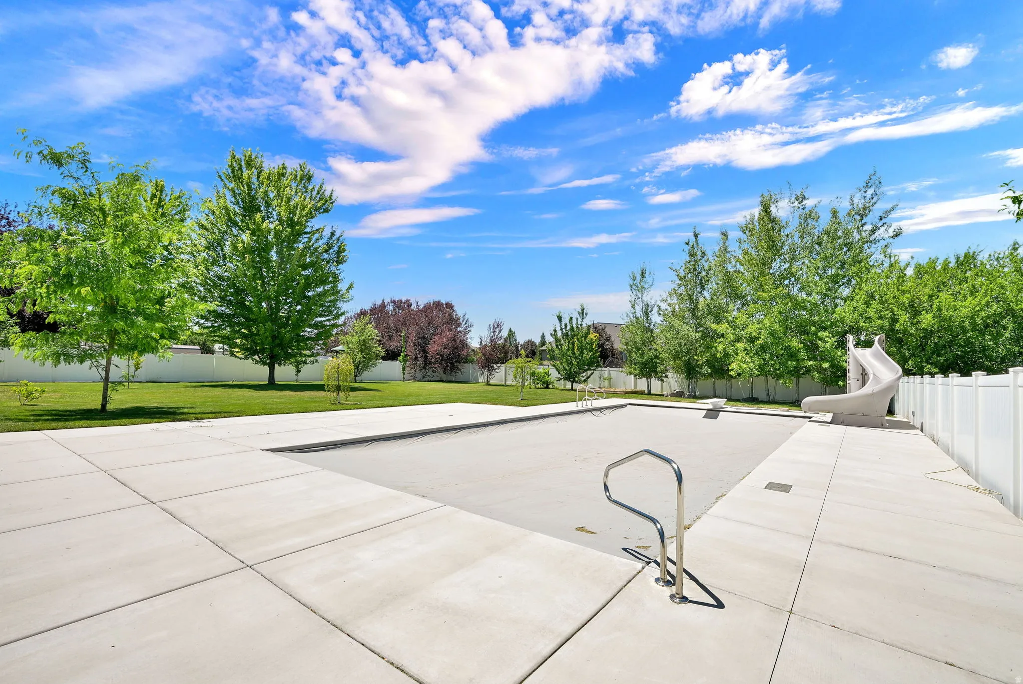 Expansive outdoor space featuring a covered swimming pool, a dedicated pool slide, and a surrounding concrete deck