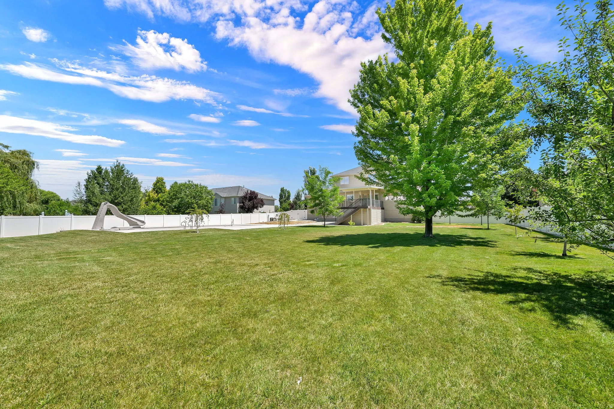 Expansive Half Acre lawn with mature trees, perimeter fencing, and a terraced rear exterior