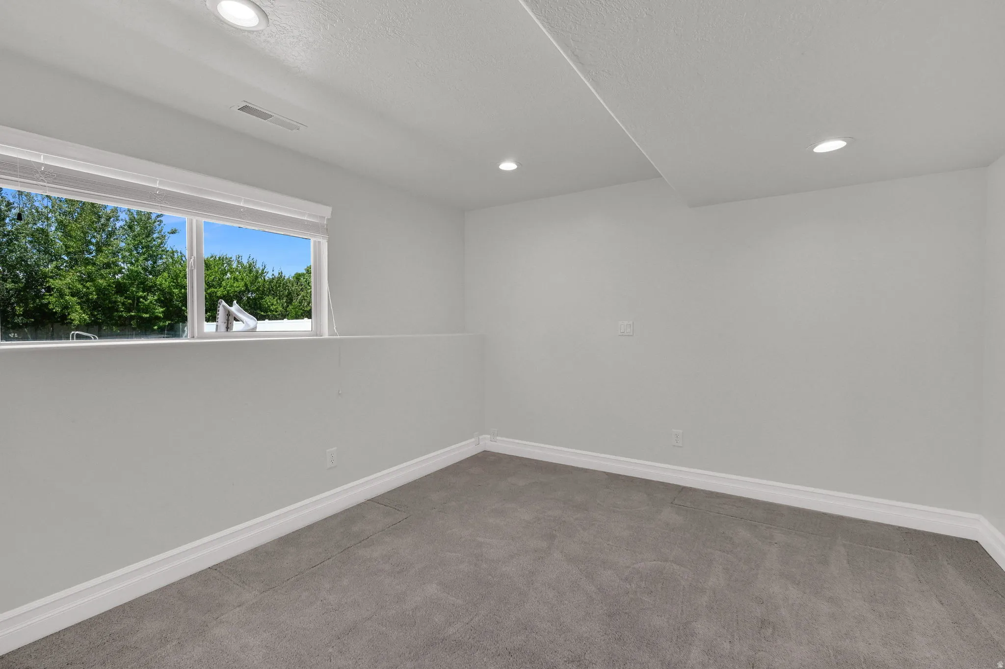 Carpeted bedroom with a large window, white trim, recessed lighting, and light gray walls