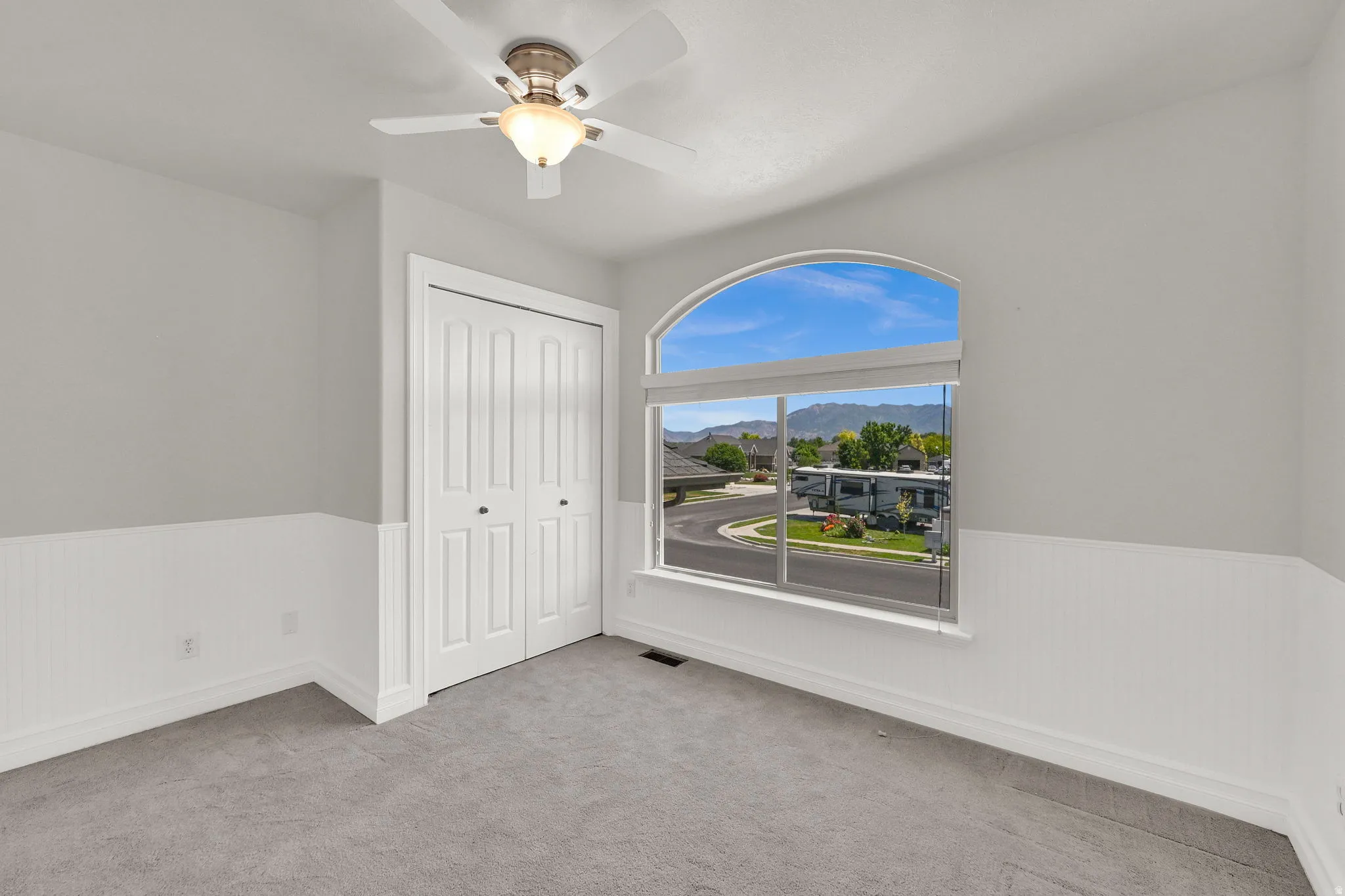 Room featuring a large arched window with mountain scenery, a ceiling fan with integrated lighting, and a closet with bifold doors