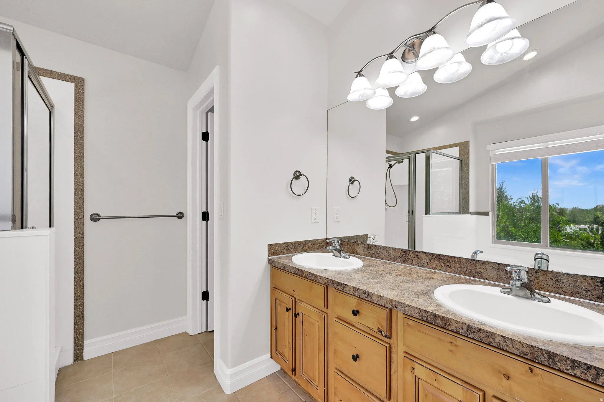 Bathroom featuring a dual vanity with light wood cabinetry and a brown-patterned countertop