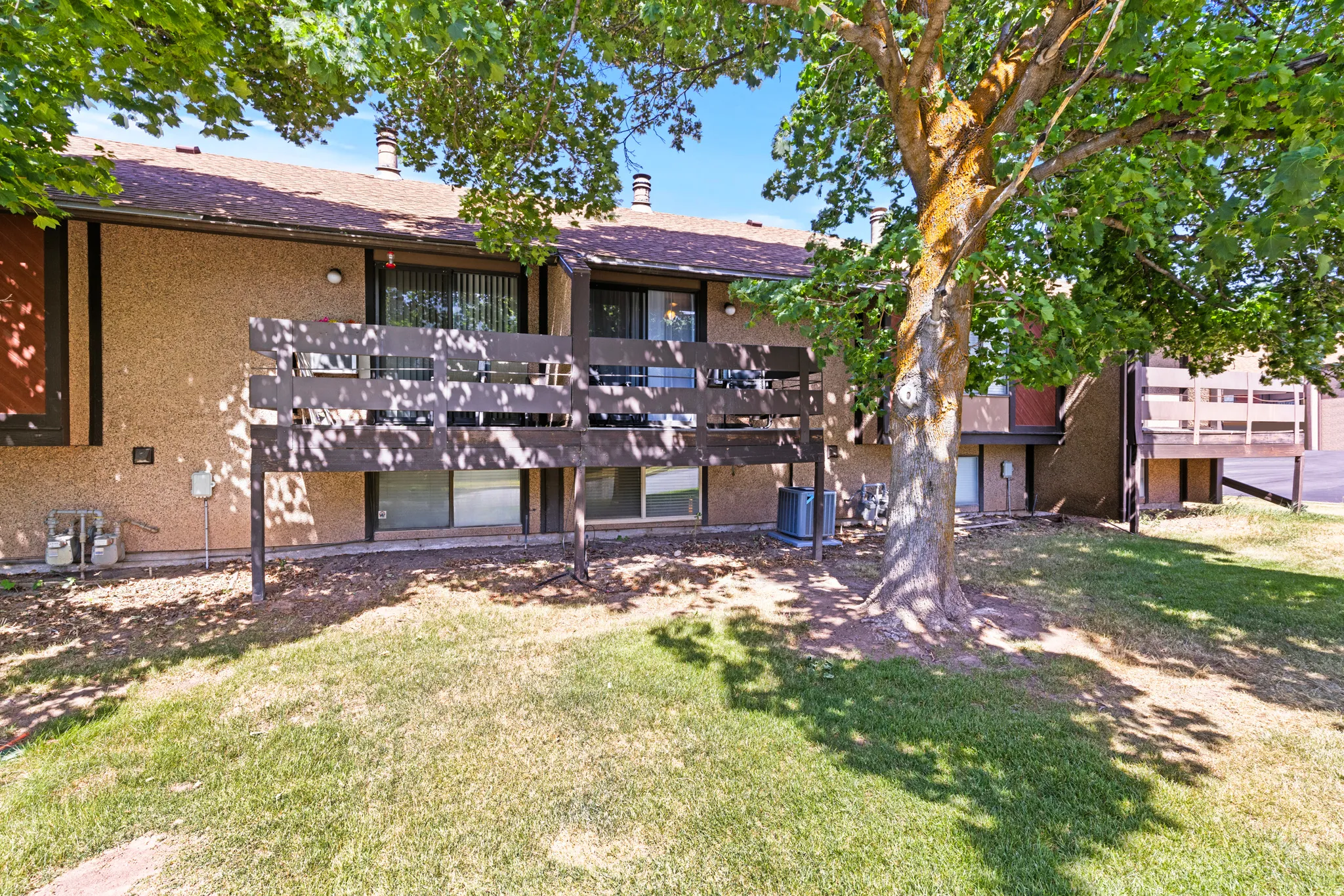 Townhome exterior featuring a private deck with wooden railing, stucco siding, and a shingled roof