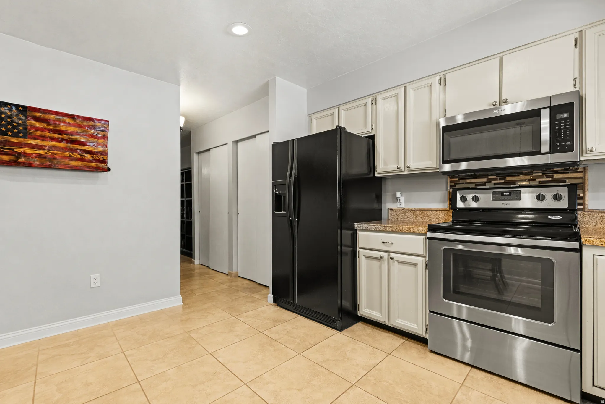 Kitchen featuring stainless steel appliances, light-toned cabinetry, granite-style countertops, and a decorative tile backsplash