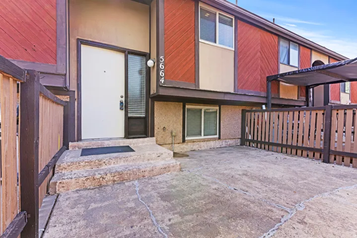 Multi-level exterior with red wood-finish siding, textured stucco, and a white entry door with a frosted sidelight