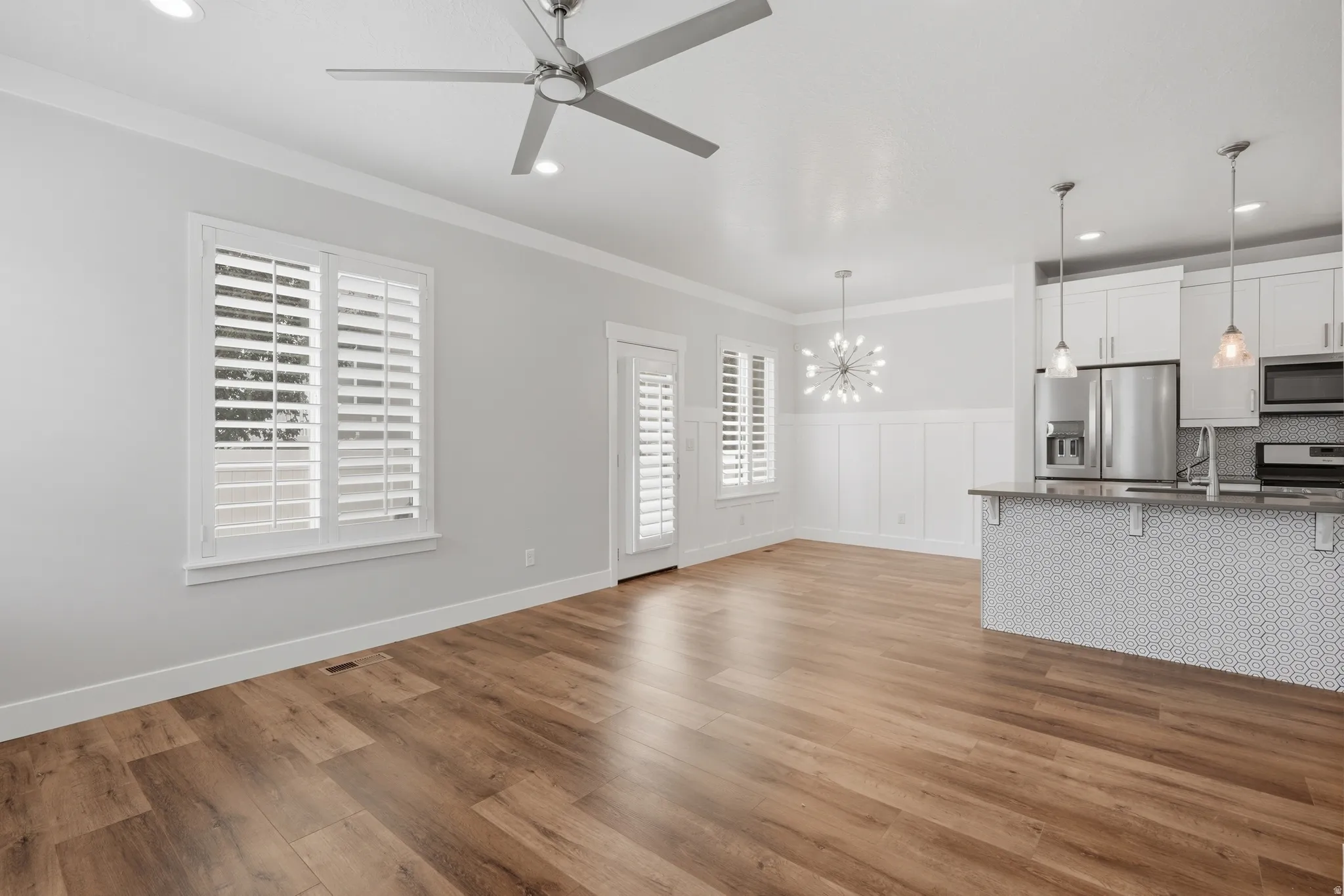 Open-concept living area featuring wood-finish flooring, white plantation shutters, and a modern ceiling fan