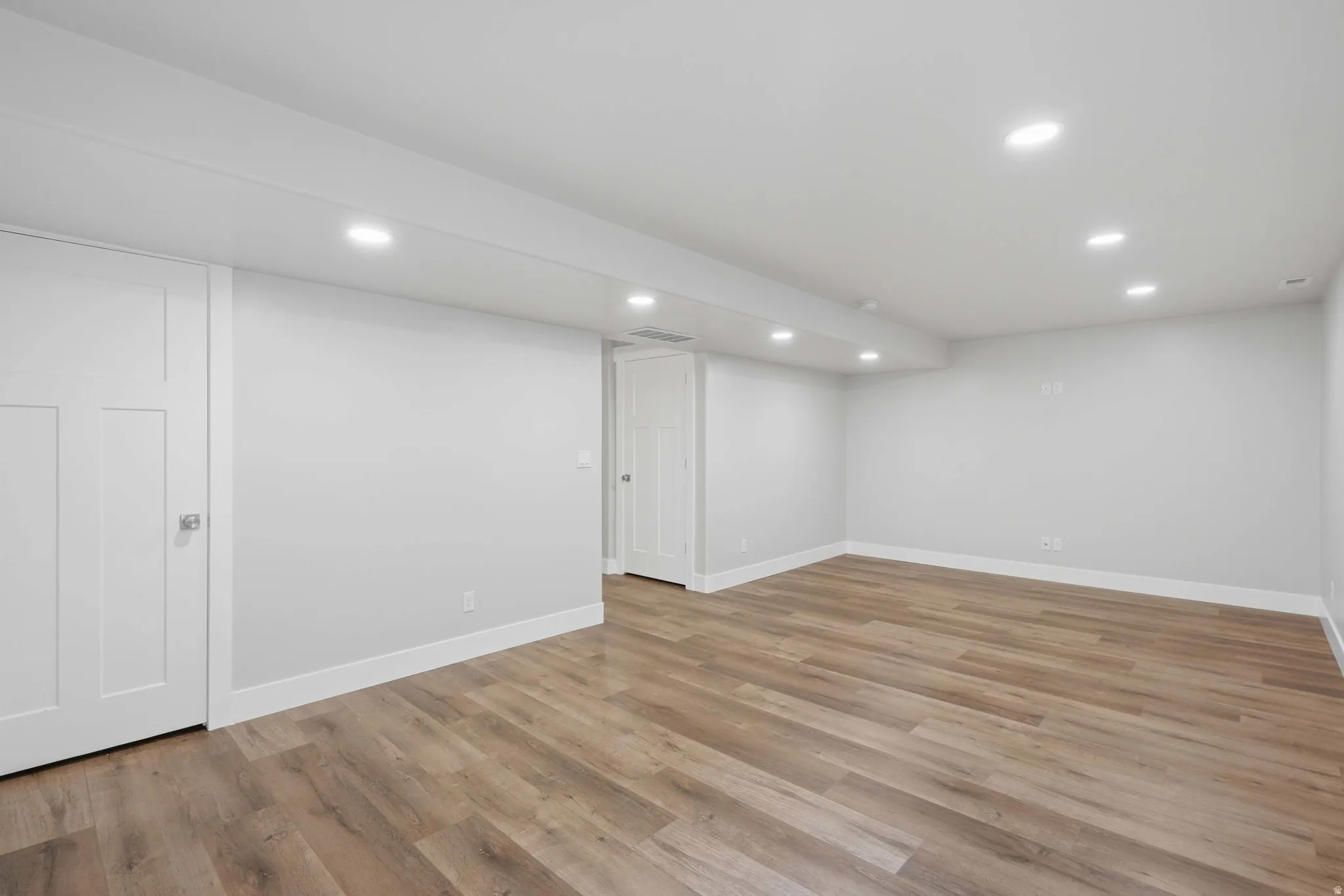 Spacious interior room featuring wood-finish flooring, light gray walls, and recessed ceiling lighting