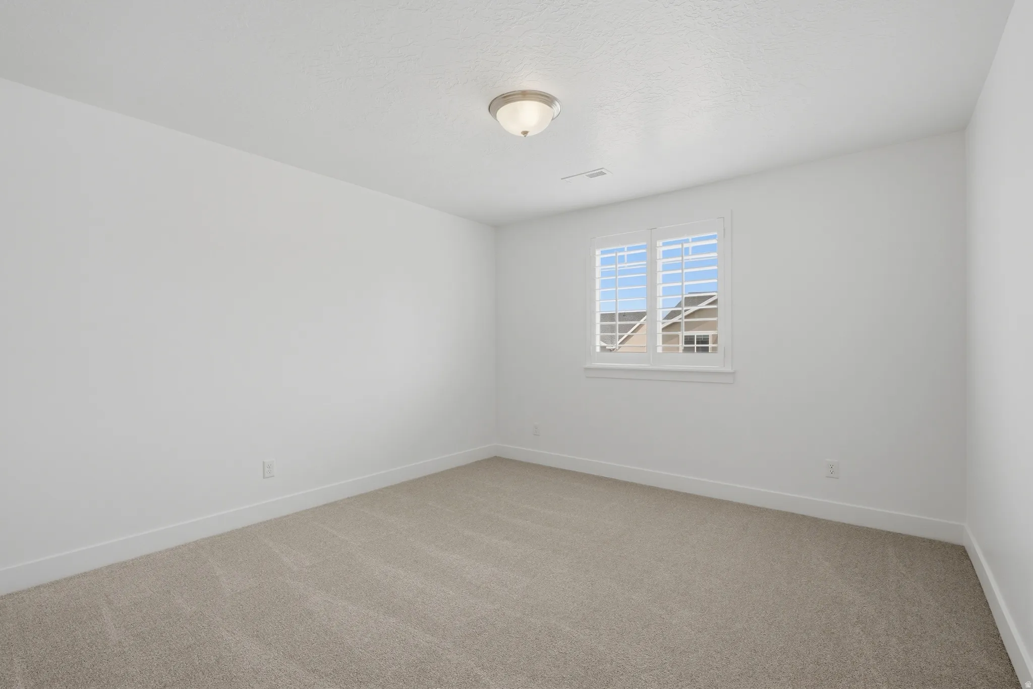 Neutral color palette with textured carpeting, white walls, and a window featuring plantation shutters