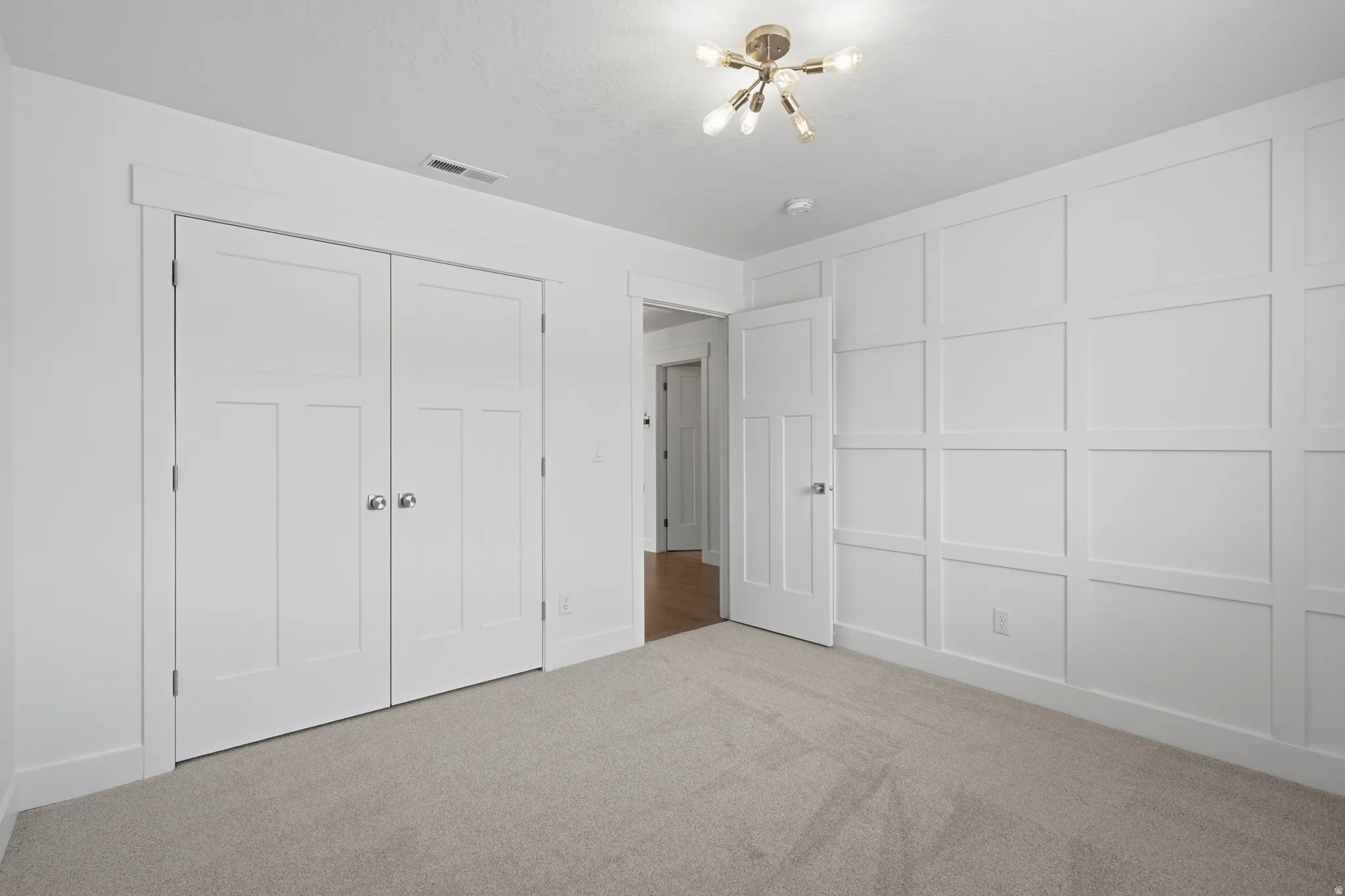 Bedroom featuring neutral carpeting, a decorative wall panel accent, a modern ceiling light fixture, and white bi-fold closet doors